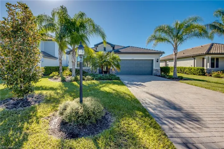 View of front of home with stone siding, decorative driveway, stucco siding, an attached garage, and a front lawn