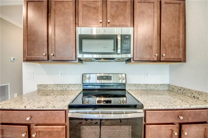 Kitchen with stainless steel appliances, light stone counters, ornamental molding, and brown cabinetry