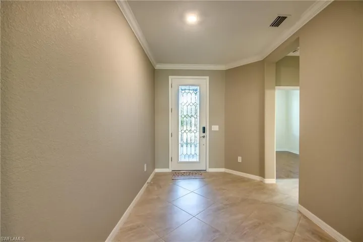 Entryway with ornamental molding, light tile patterned floors, and a textured wall