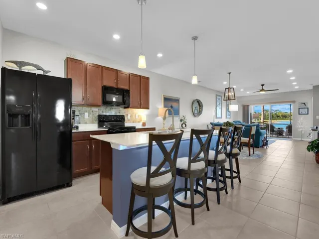 Kitchen featuring ceiling fan, black appliances, a center island with sink, hanging light fixtures, and light tile patterned flooring