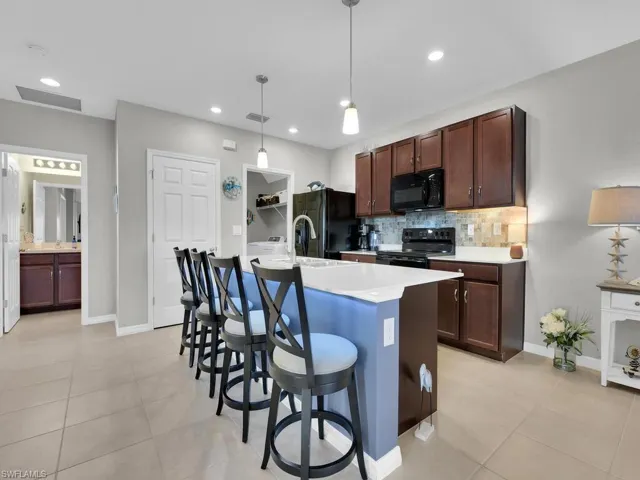 Kitchen featuring decorative backsplash, a breakfast bar, a kitchen island with sink, black appliances, and decorative light fixtures
