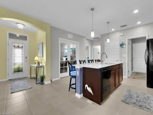 Kitchen with sink, pendant lighting, a center island with sink, light tile patterned floors, and black appliances