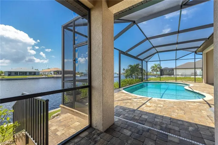 View of pool with glass enclosure, a water view, and a patio