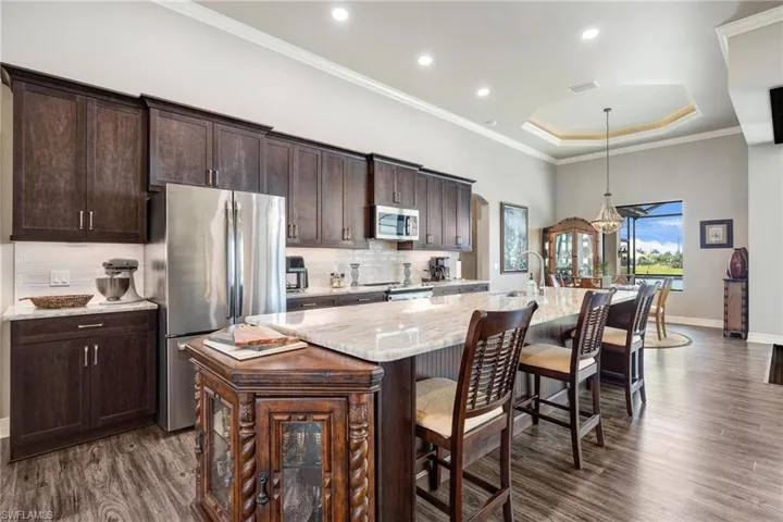 Kitchen featuring stainless steel appliances, a kitchen island with sink, decorative light fixtures, tasteful backsplash, and dark hardwood / wood-style flooring
