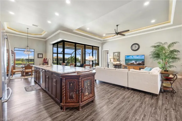 Kitchen with a raised ceiling, ceiling fan with notable chandelier, dark hardwood / wood-style flooring, an island with sink, and decorative light fixtures