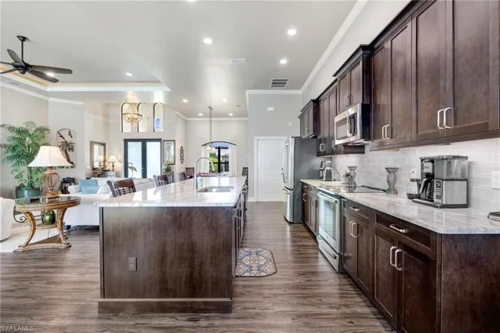 Kitchen featuring ceiling fan, appliances with stainless steel finishes, dark hardwood / wood-style flooring, and a kitchen island with sink