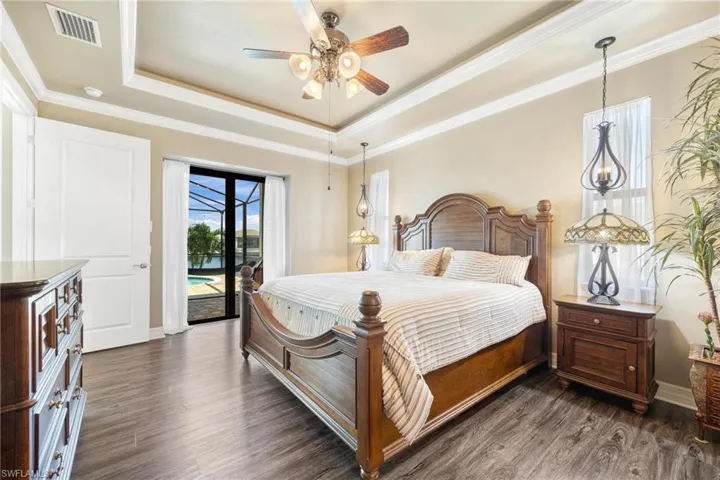 Primary Bedroom with a raised ceiling, ornamental molding, ceiling fan, dark hardwood / wood-style floors, and access to exterior