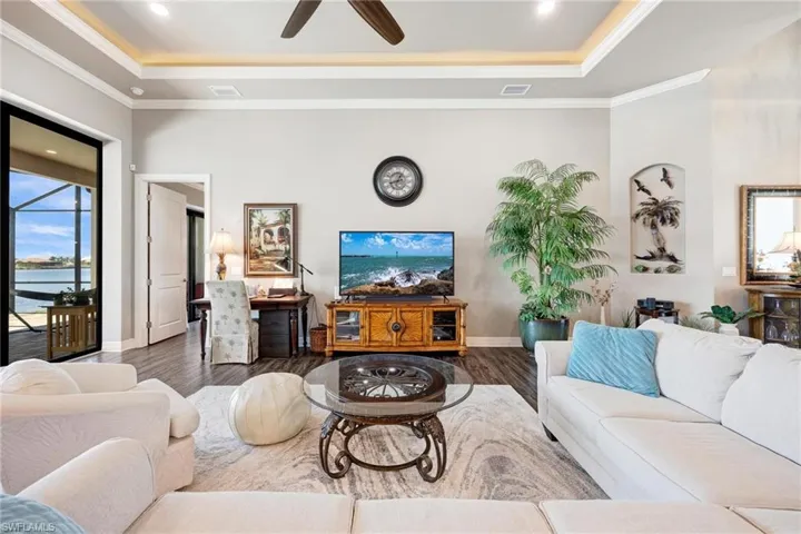 Living room with ceiling fan, dark hardwood / wood-style floors, a tray ceiling, and crown molding