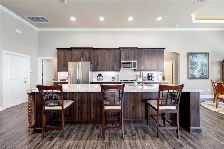 Kitchen with a breakfast bar, appliances with stainless steel finishes, dark hardwood / wood-style flooring, and a kitchen island with sink