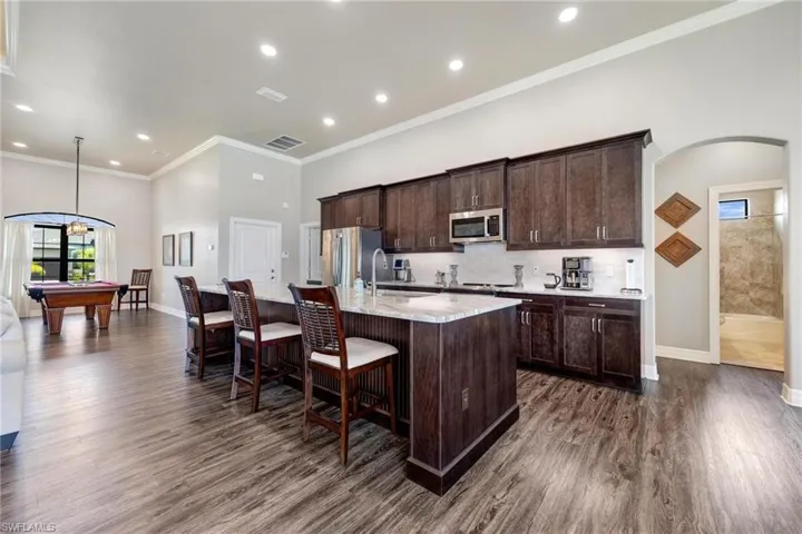 Kitchen with pool table, dark wood-type flooring, stainless steel appliances, and a kitchen island with sink