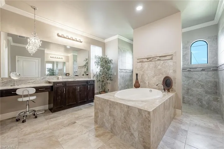 Primary Bathroom featuring tile patterned floors, ornamental molding, tiled tub, and vanity