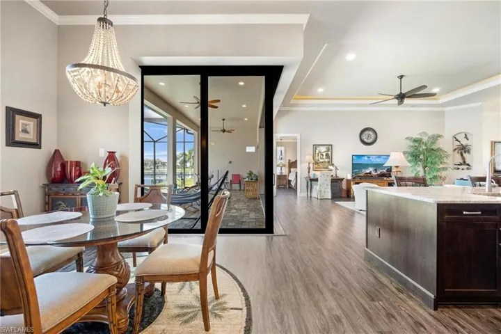Dining space with sink, hardwood / wood-style flooring, ceiling fan with notable chandelier, and a tray ceiling