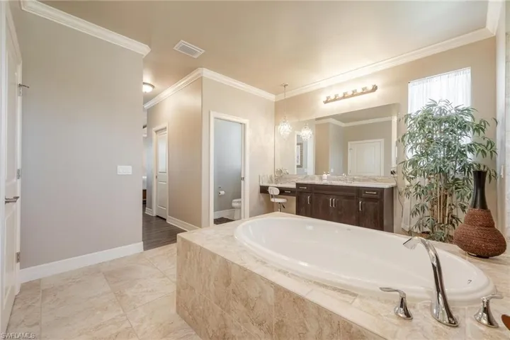 Primary Bathroom with toilet, tiled bath, tile patterned floors, ornamental molding, and vanity