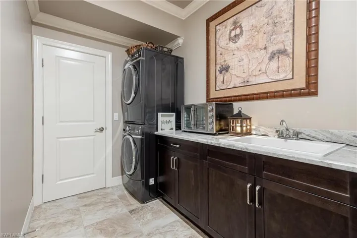 Laundry area with light tile patterned flooring, ornamental molding, stacked washing maching and dryer, and sink
