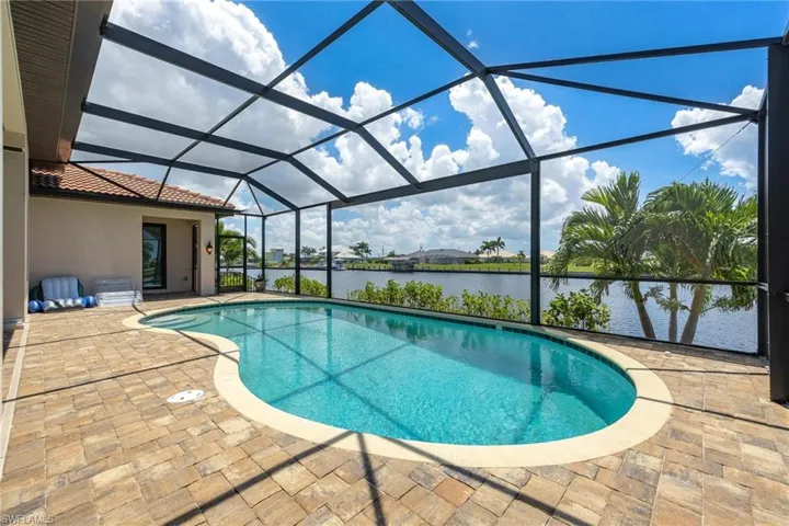 View of pool with glass enclosure, a water view, and a patio area