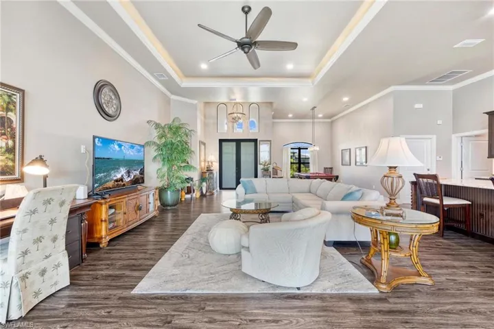 Living room with ceiling fan, a raised ceiling, ornamental molding, and dark hardwood / wood-style floors