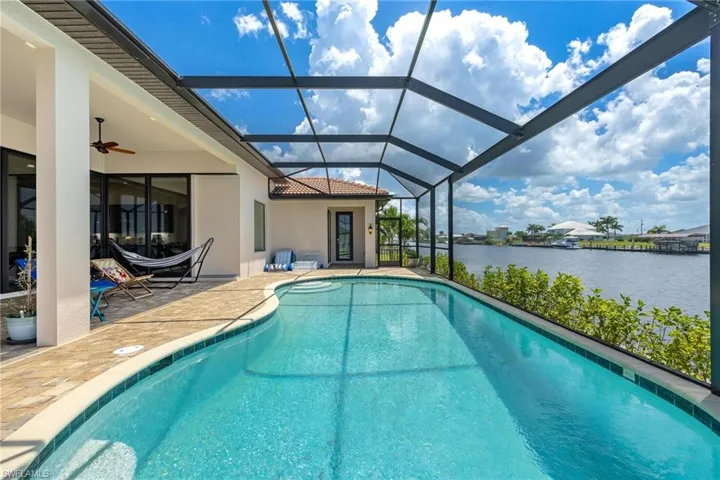 View of pool with ceiling fan, a patio, a water view, and a lanai