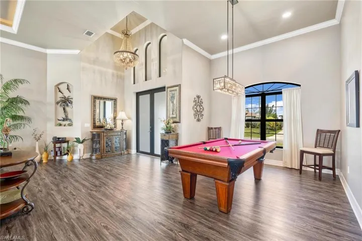 Recreation room with a towering ceiling, pool table, dark hardwood / wood-style flooring, and crown molding