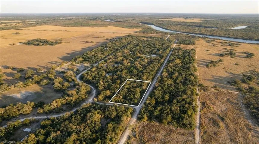 Expansive land parcel featuring dense tree coverage, a natural waterway in the distance, and surrounding open fields