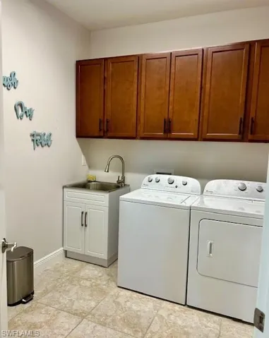 Clothes washing area with independent washer and dryer, sink, light tile floors, and cabinets