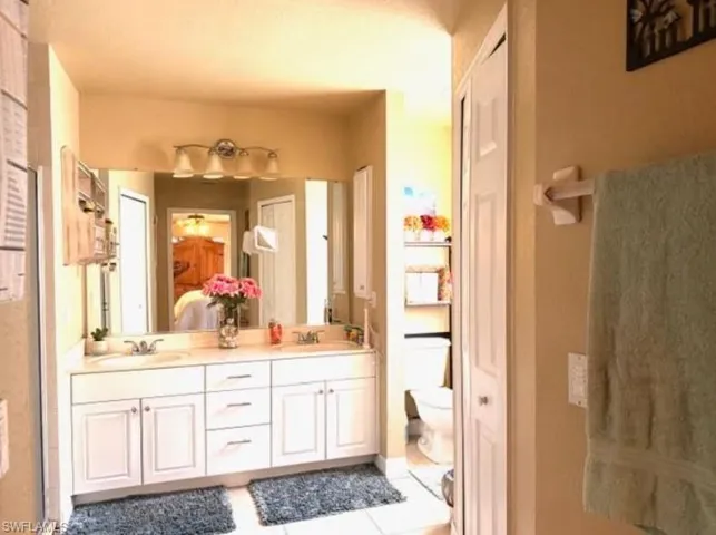 Ensuite bathroom featuring double vanity, a shower stall, light tile patterned floors, and a closet
