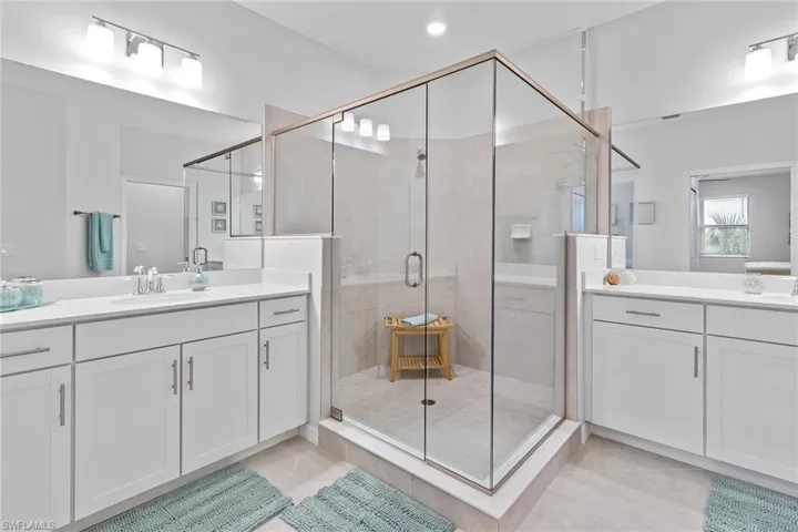 Bathroom featuring double vanity with extensive cabinet space, tile floors, and a glass shower with door.