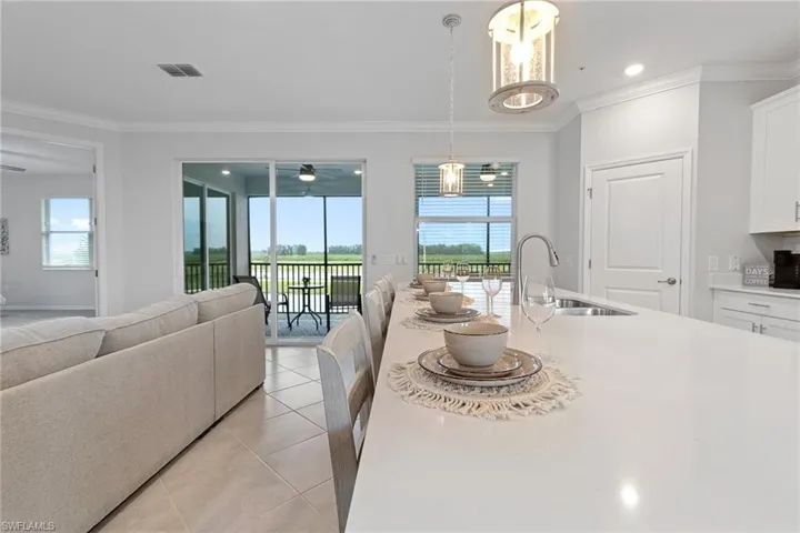 Kitchen featuring white cabinetry, hanging light fixtures, ornamental molding, sink, and light tile floors
