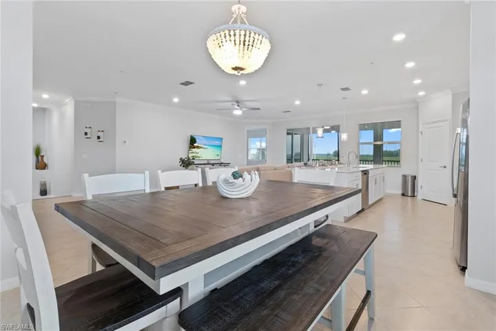 Tiled dining space with sink, crown molding, and ceiling fan with notable chandelier