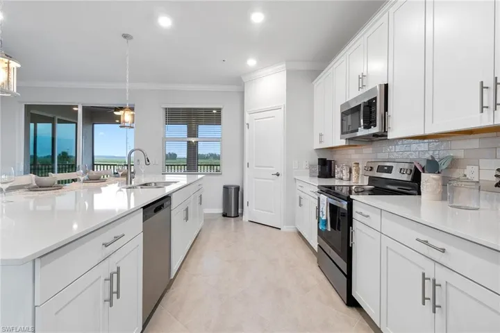 Kitchen with stainless steel appliances, light tile flooring, backsplash, sink, and white cabinetry