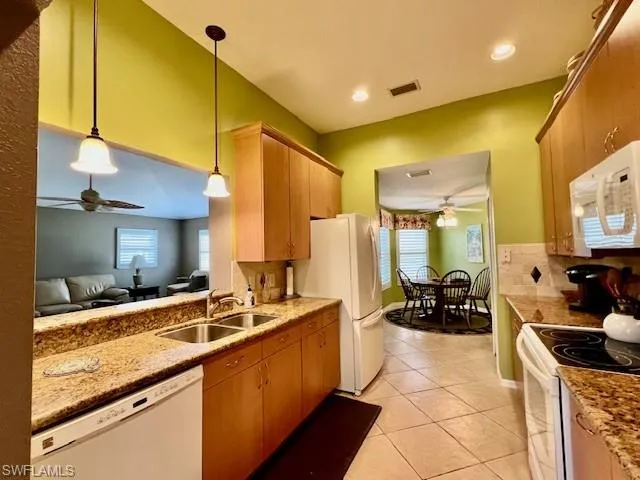 Kitchen featuring white appliances, hanging light fixtures, light tile patterned flooring, ceiling fan, and sink