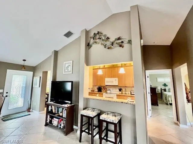 Kitchen with white appliances, kitchen peninsula, light brown cabinetry, decorative light fixtures, and lofted ceiling