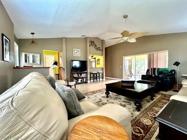 Living room with a textured ceiling, tile patterned floors, ceiling fan, and vaulted ceiling