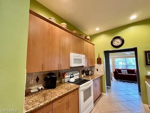 Kitchen featuring white appliances, light stone countertops, tasteful backsplash, and light tile patterned floors