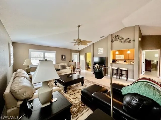Living room featuring lofted ceiling, ceiling fan, and light tile patterned floors