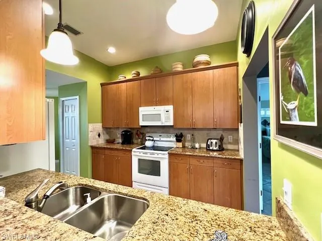 Kitchen with white appliances, sink, tasteful backsplash, and hanging light fixtures