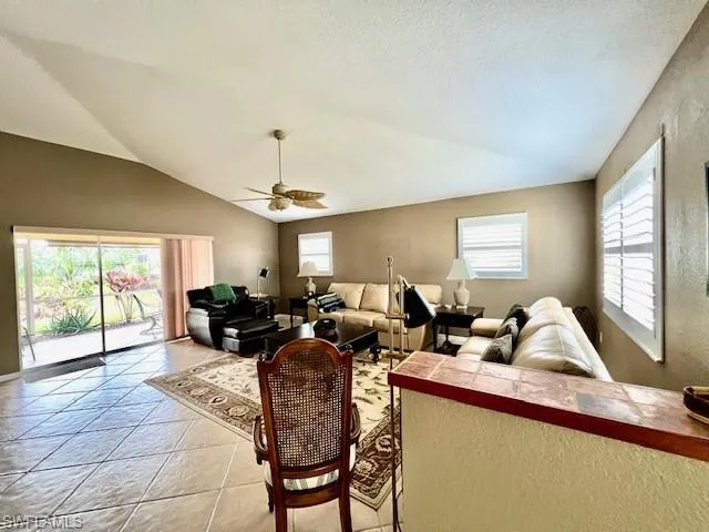 Tiled living room featuring ceiling fan, a textured ceiling, a healthy amount of sunlight, and vaulted ceiling