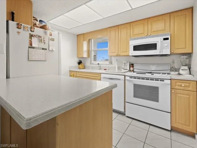 Kitchen featuring a center island, light brown cabinetry, light tile patterned flooring, and white appliances