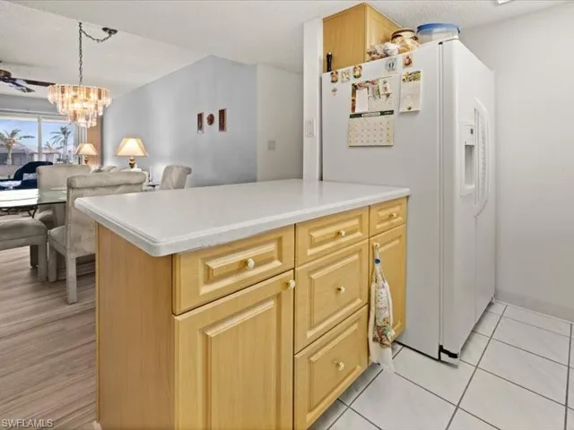 Kitchen featuring light brown cabinets, white refrigerator with ice dispenser, an inviting chandelier, hanging light fixtures, and light tile patterned floors
