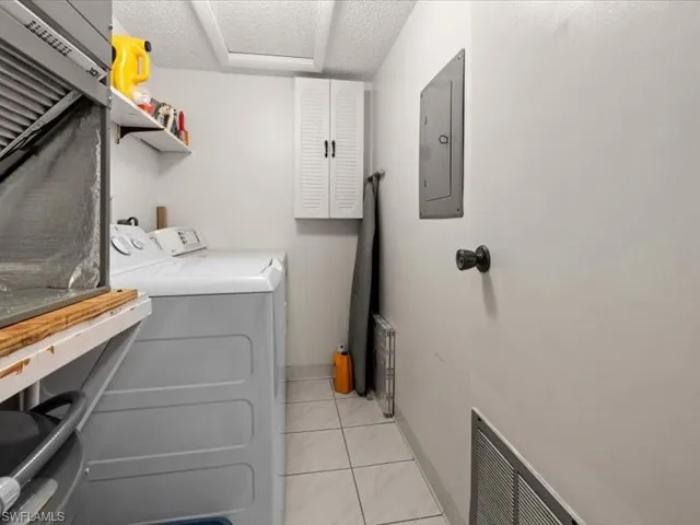 Laundry area featuring light tile patterned floors, washing machine and dryer, electric panel, and a textured ceiling