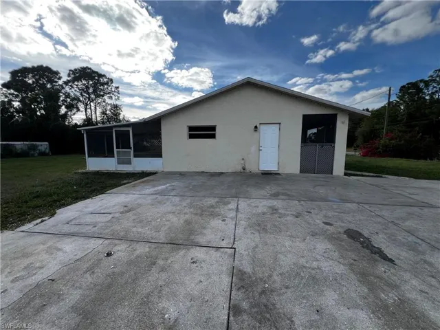 Rear view of house featuring a sunroom, concrete driveway, stucco siding, and a lawn