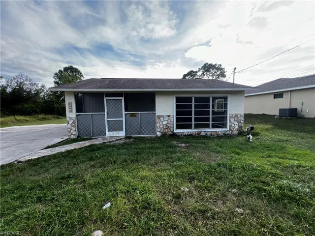 View of front of home featuring a front lawn, cooling unit, stone siding, and stucco siding