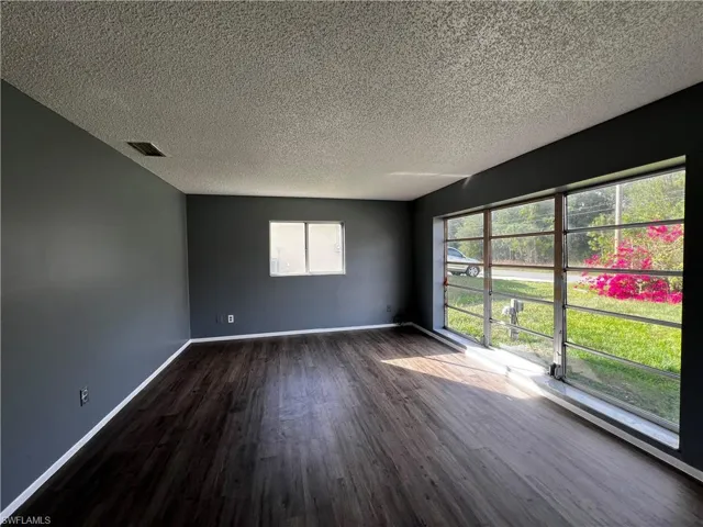 Unfurnished room with dark wood finished floors, baseboards, visible vents, and a textured ceiling