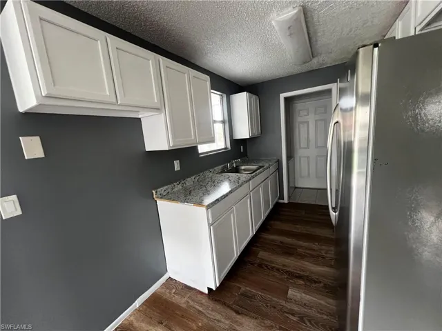 Kitchen featuring a textured ceiling, dark wood finished floors, white cabinetry, a sink, and freestanding refrigerator