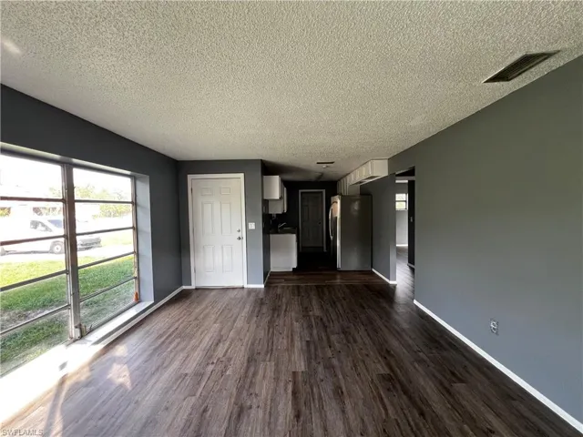 Unfurnished living room featuring dark wood-type flooring, baseboards, a textured ceiling, and visible vents