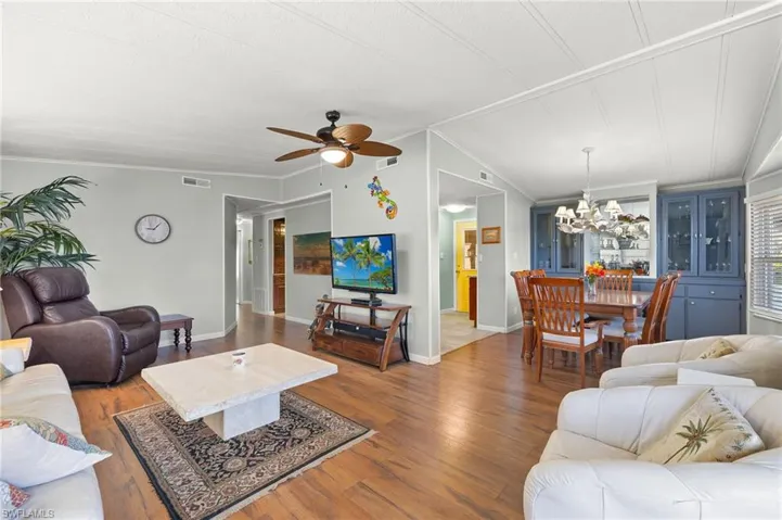 Living room with hardwood / wood-style flooring, ceiling fan with notable chandelier, lofted ceiling, and crown molding