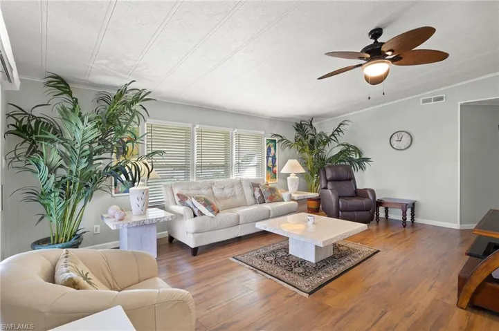 Living room featuring ceiling fan, dark wood-type flooring, a textured ceiling, and ornamental molding