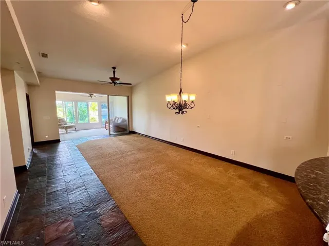 Empty room featuring stone tile flooring, vaulted ceiling, baseboards, visible vents, and ceiling fan with notable chandelier