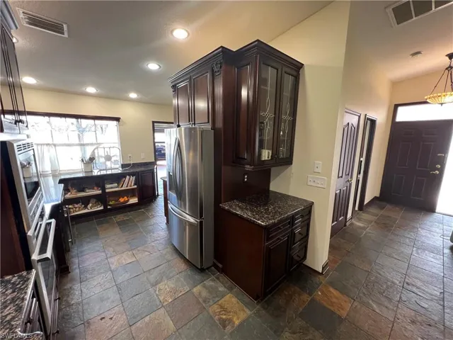 Kitchen featuring stone tile flooring, visible vents, dark brown cabinetry, and stainless steel fridge with ice dispenser