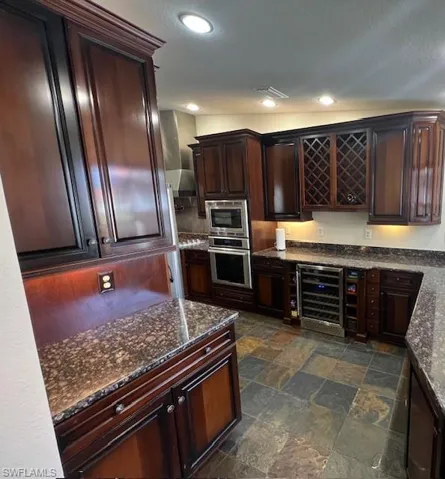 Kitchen with stone finish floor, dark stone countertops, stainless steel appliances, and wine cooler