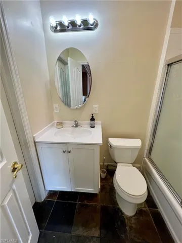 Full bathroom with baseboards, vanity, bath / shower combo with glass door, and toilet
